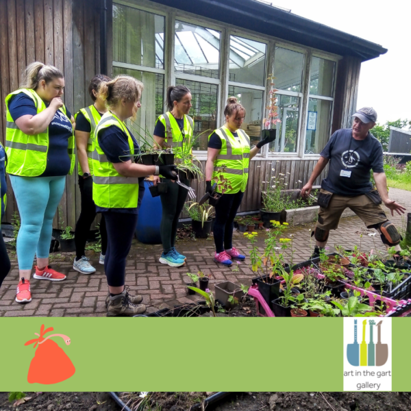 A group of people with light skin tone, wearing high vis jackets, standing in a garden space in front of growing plots. Logo: Art in the Gart